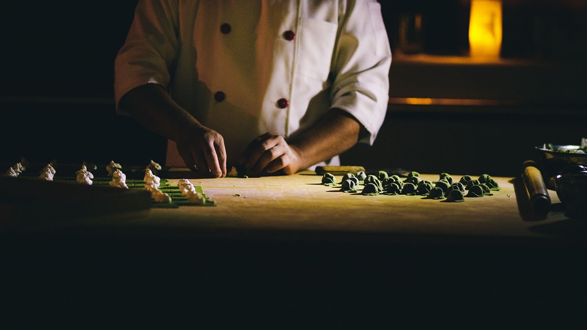 Chef artigiano che prepara pasta fresca in una cucina semibuia