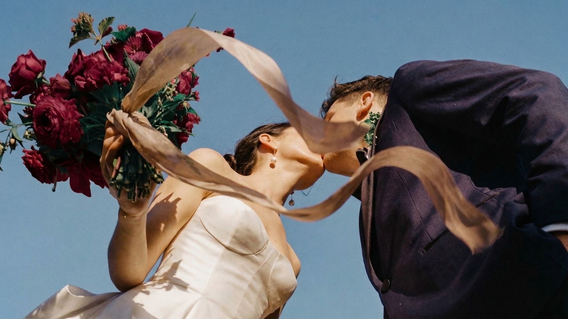 Sposi che si baciano durante la cerimonia, bouquet di rose bordeaux